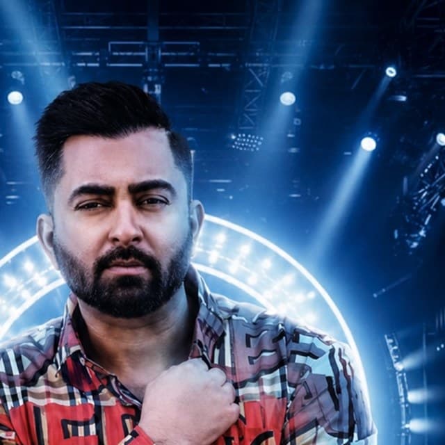Sharry Mann in a checked shirt, hand to his chest, blue stage lights behind him