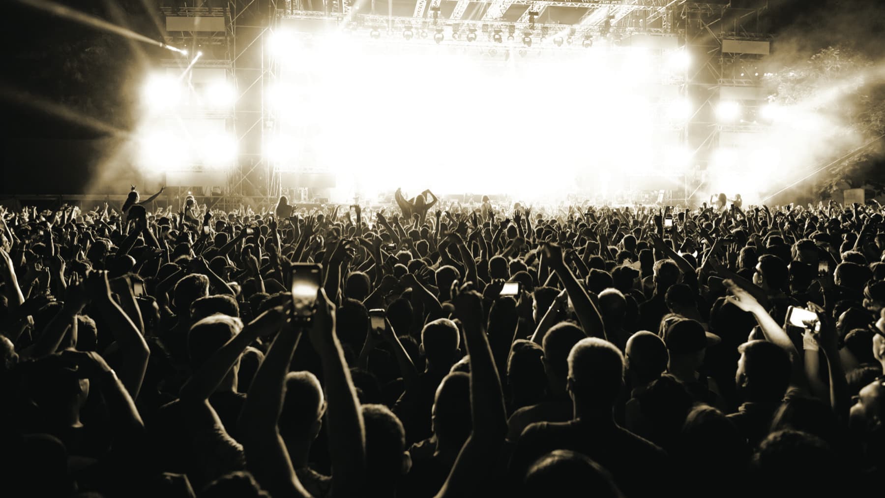 A packed arena of festival-goers under white stage beams