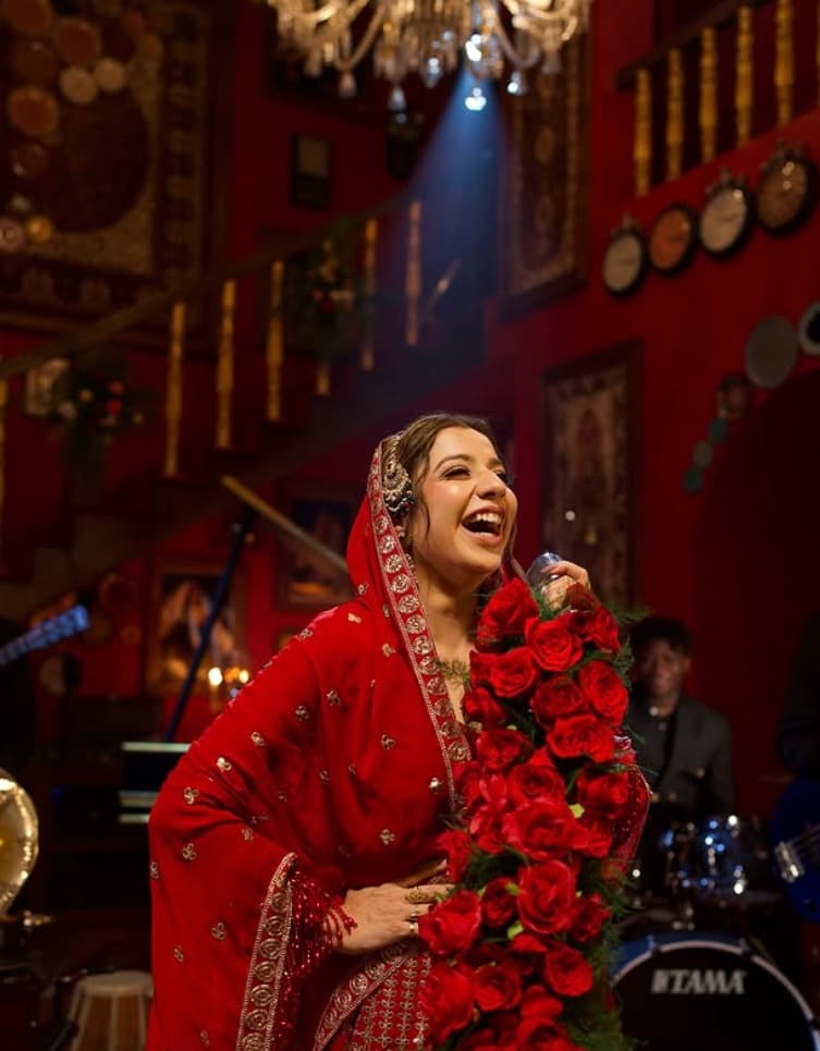 Jasmine Sandlas performing in a red saree, mic in hand, roses across the stage
