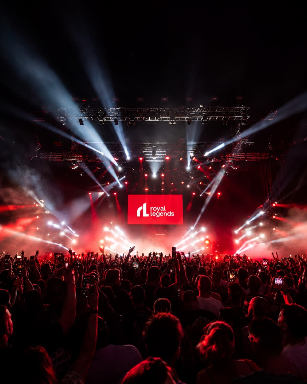 Arena crowd with phones raised toward a Royal Legends screen above a stage lit by red and white beams