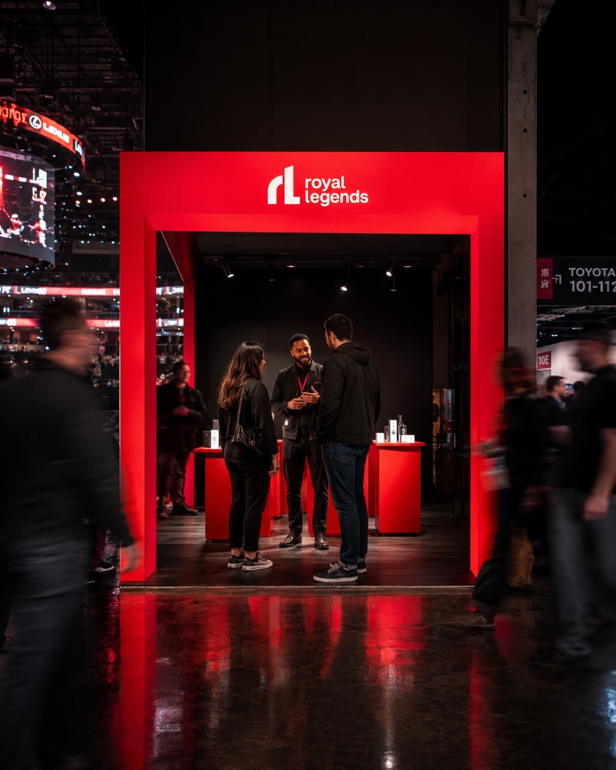 A red Royal Legends activation portal on an arena concourse, hosts talking with two guests inside