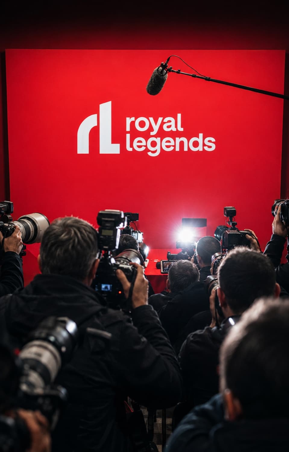A press pack shooting a red Royal Legends media wall, boom mic overhead and flashes firing